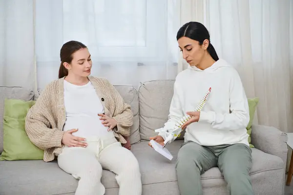 Una mujer embarazada y su entrenador se sientan en un sofá, mirando atentamente el modelo anatómico, los cursos de los padres. - foto de stock