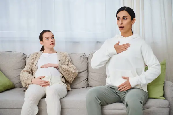 Две беременные женщины сидят вместе на диване, одна получает руководство от своего инструктора во время родительского курса. — стоковое фото