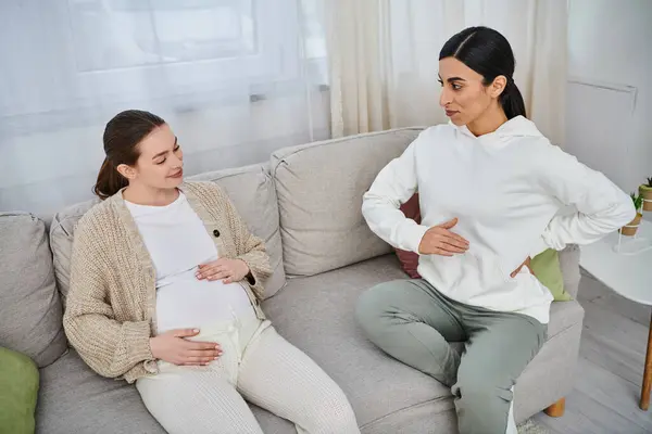 Una donna incinta siede su un divano accanto al suo allenatore durante i corsi dei genitori, rispecchiandosi a vicenda.. — Foto stock