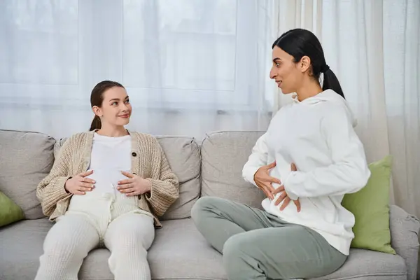 Dos mujeres, una embarazada, que participan en una conversación profunda en un sofá acogedor durante los cursos de padres. - foto de stock