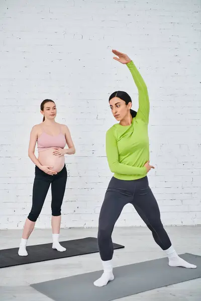 Dos mujeres embarazadas que participan en una sesión de yoga calmante dirigida por un instructor durante un curso prenatal. - foto de stock