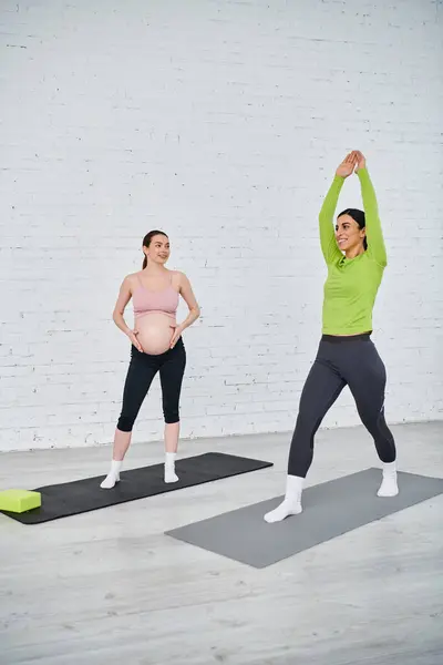 Dos mujeres embarazadas practican yoga juntas con gracia bajo la guía de un entrenador en una clase prenatal. - foto de stock