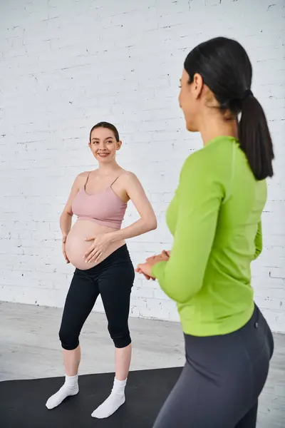 A pregnant woman stands confidently in front of a white brick wall with her coach during a parents course. — Stock Photo