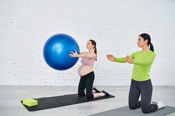 Madre embarazada ejercicio con gracia con una pelota durante una clase de fitness prenatal, guiada por su entrenador. - foto de stock