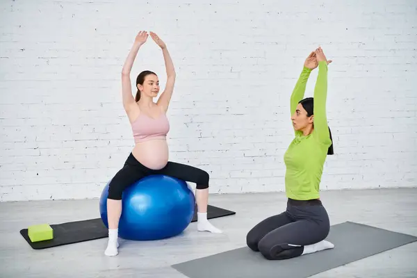 Mujer embarazada con gracia realizar posturas de yoga en grandes bolas de ejercicio bajo la guía de su instructor. - foto de stock