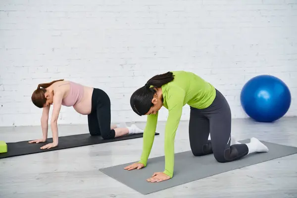 Deux femmes, une enceinte, debout gracieusement sur des tapis de yoga, s'engageant dans une routine d'étirement sereine et concentrée. — Photo de stock