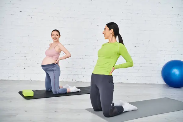 Mujer embarazada con gracia participar en el yoga posa en un gimnasio bajo la guía de su instructor durante las clases prenatales. - foto de stock