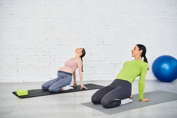 Una mujer embarazada está practicando yoga con su entrenador en una sala serena, centrándose en movimientos conscientes y técnicas de respiración.. - foto de stock