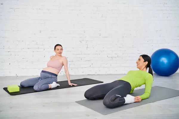 Una mujer embarazada y su entrenador participan en una sesión de yoga pacífica sobre esteras, que encarna la fuerza y la gracia. - foto de stock