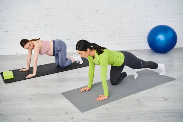 Dos mujeres en colchonetas de yoga haciendo flexiones, una de las cuales está embarazada, recibiendo orientación de un entrenador durante los cursos de los padres. - foto de stock