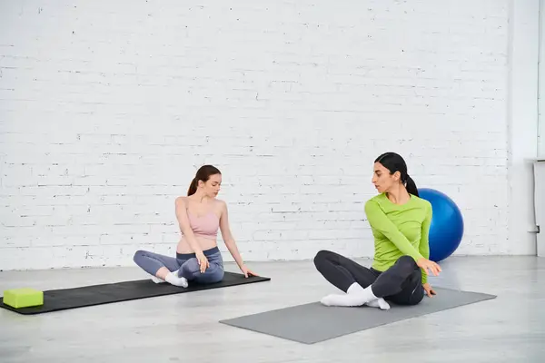 Una mujer embarazada hace ejercicios con su entrenador durante un curso de padres, sentada en colchonetas de yoga en un entorno sereno. - foto de stock