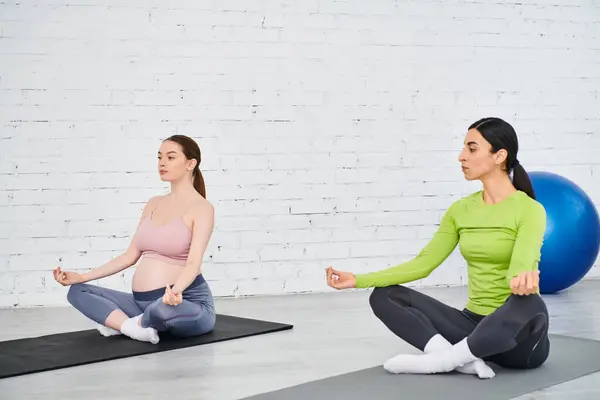 Dos mujeres se sientan en colchonetas de yoga, comprometidas en una sesión pacífica. - foto de stock