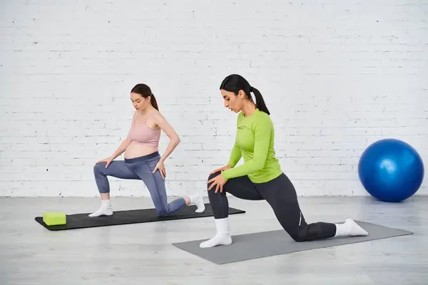 Две женщины, одна беременная, стоят вместе на коврике для йоги, участвуя в упражнениях по поддержанию равновесия и укреплению сил.. — стоковое фото