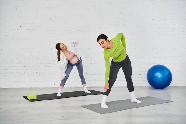 Ein Trainer und eine schwangere Frau führen während eines Elternkurses Yoga-Übungen auf Matten durch. — Stockfoto