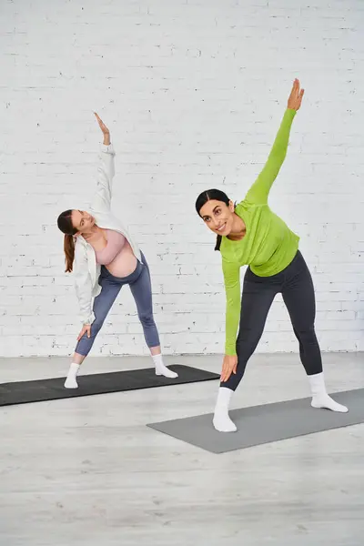A pregnant woman gracefully practices yoga with her instructor in a serene studio setting. — Stock Photo