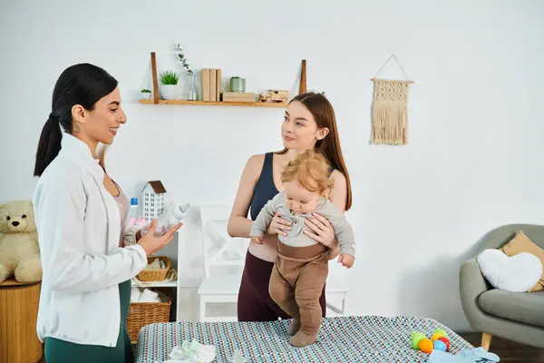 A young, beautiful mother tenderly holds her baby in her arms at home, guided by her coach from parents courses. — Stock Photo