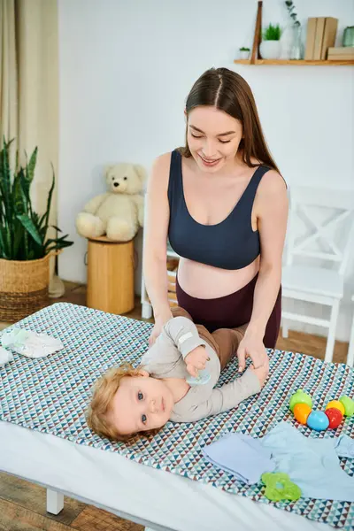 Una madre joven y hermosa interactúa alegremente con su bebé en una cama acogedora, entrenador de crianza. - foto de stock
