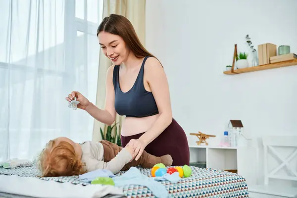 A young mother in a bra top joyfully plays with her baby, parents course at home. — Stock Photo