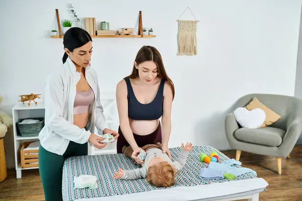 A young, beautiful mother stands next to her baby on a cozy bed, receiving guidance from a parenting coach during a home visit. — Stock Photo