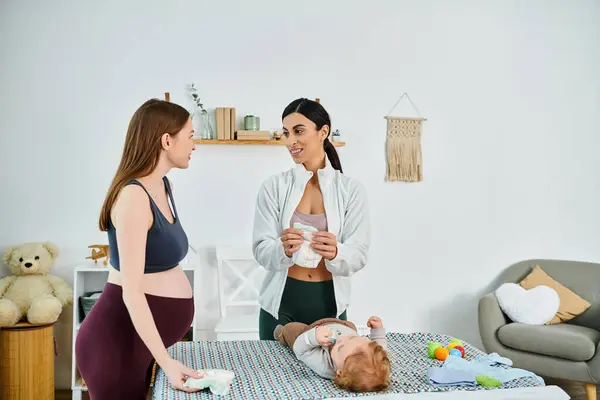 Eine junge Mutter steht liebevoll neben ihrem Baby, das auf einem Bett liegt, unterstützt von ihrem Trainer aus Elternkursen.. — Stockfoto