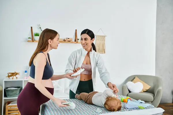 A young beautiful mother lovingly stands next to her baby on a bed, receiving guidance from her coach at parents courses. — Stock Photo