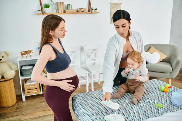 A beautiful young mother stands next to a baby on a bed, receiving guidance from her coach at parents courses. — Stock Photo