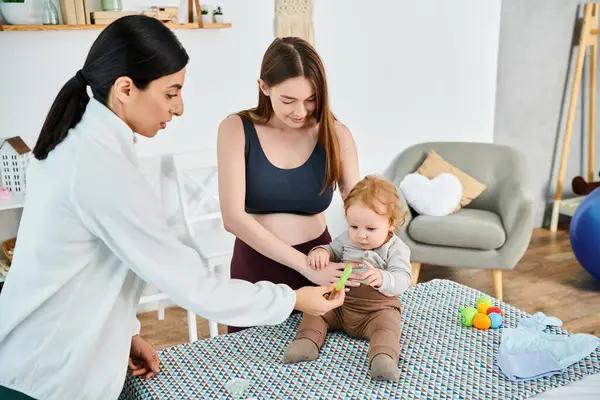 A young mother engages in playful interaction with her baby in a cozy room, supported by her coach from parents courses. — Stock Photo