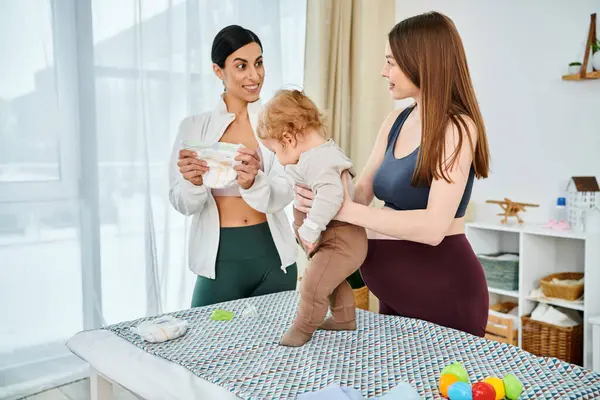 Uma jovem mãe embala seu bebê enquanto recebe orientação de um treinador parental, tanto fomentando o amor quanto o apoio em casa.. — Fotografia de Stock