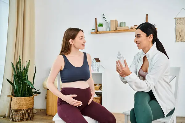 Una mujer se sienta en una silla, hablando con una mujer embarazada, compartiendo sabiduría y apoyo en un curso de padres. - foto de stock
