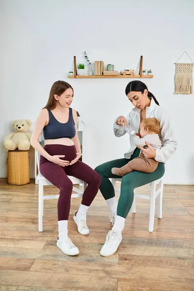 A pregnant woman sits, cradling her newborn, receiving guidance from a coach at a parents course at home. — Stock Photo
