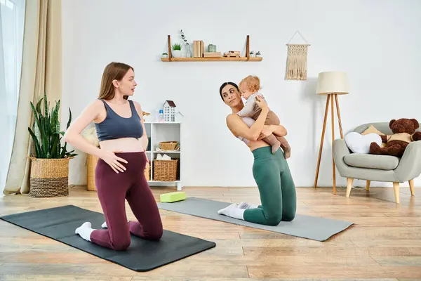 Una madre joven sostiene con gracia a su bebé mientras está de pie en una esterilla de yoga durante una sesión de curso de padres en casa. - foto de stock