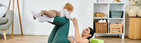 Eine junge, schöne Mutter hebt ihr Baby freudig in die Luft, während sie bei Elternkursen von einem Trainer angeleitet wird. — Stockfoto