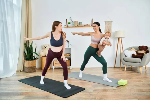 Una madre joven y hermosa y su bebé practicando yoga en una acogedora sala de estar con la guía de su instructor durante los cursos para padres. - foto de stock