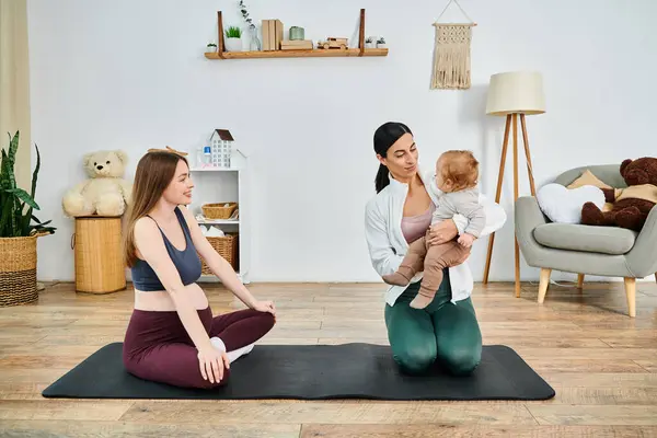 Une jeune mère s'assoit sur un tapis de yoga, berçant son bébé dans ses bras, tandis que son entraîneur la guide à travers de doux exercices lors d'un cours de parents. — Photo de stock
