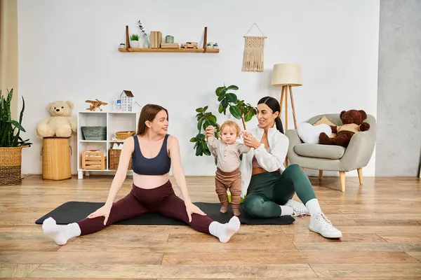 Una joven y hermosa madre se sienta en una esterilla de yoga, acunando a su bebé, con la guía de su entrenador en los cursos de padres. - foto de stock