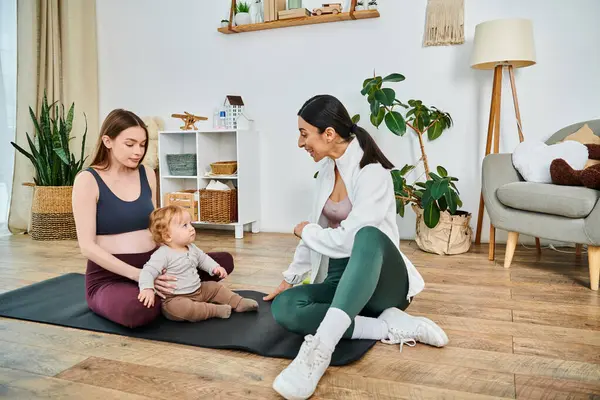 Eine junge Mutter sitzt mit ihrem Baby auf einer Yogamatte, angeleitet von ihrem Trainer bei einem Elternkurs, und sorgt für einen Moment der Ruhe und Verbundenheit. — Stockfoto