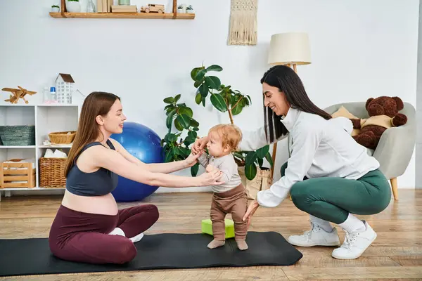 Una giovane bella madre impegnata in movimenti di yoga giocosi con il suo bambino su un tappeto, guidata da un allenatore ai corsi dei genitori. — Foto stock
