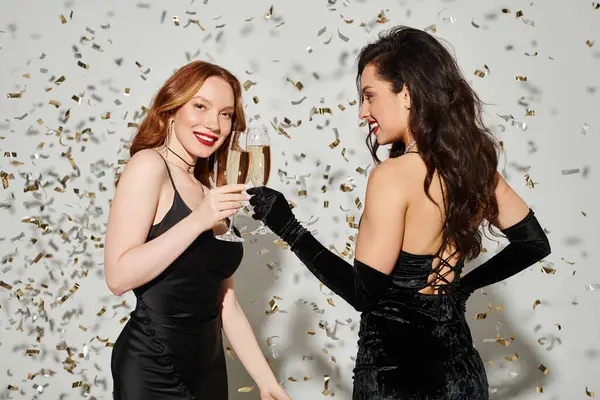 Two women in black attire joyfully hold champagne flutes. — Stock Photo