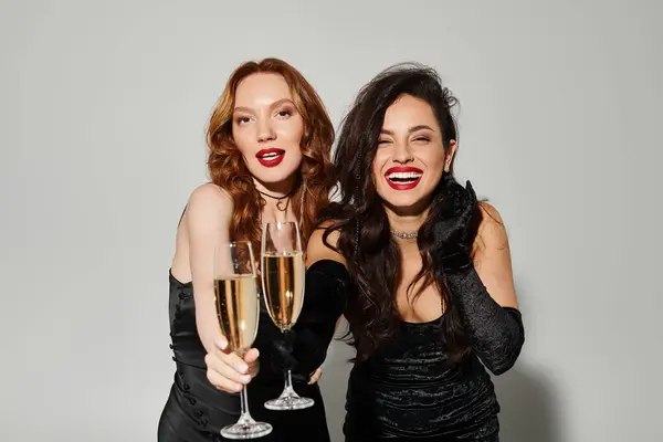 Deux femmes en robes noires clignent des verres à vin dans des toasts de fête. — Photo de stock