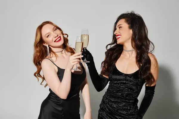 Loving lesbian couple in elegant black dresses pose joyfully with champagne flutes. — Stock Photo