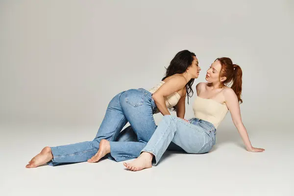 Una pareja lesbiana cariñosa con un atuendo elegante sentada en el suelo, compartiendo un momento tierno mientras una mujer toca su cara. - foto de stock