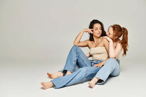 Dos mujeres en traje elegante sentadas en el suelo, los brazos alrededor de la otra en un abrazo amoroso. — Stock Photo