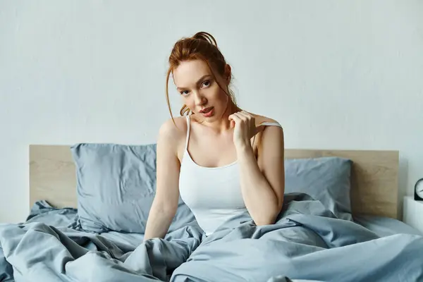 Una donna in elegante abbigliamento siede su un letto con lenzuola blu, trasudando calma. — Foto stock