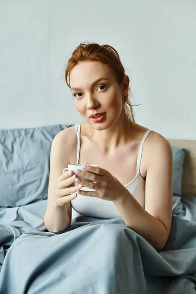 Une femme en tenue élégante s'assoit sur un lit, tenant paisiblement une tasse de café. — Photo de stock