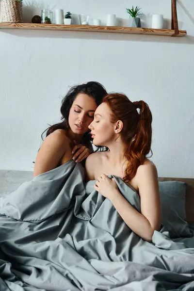 Two women in elegant attire, laying on a bed wrapped in a blanket. - foto de stock