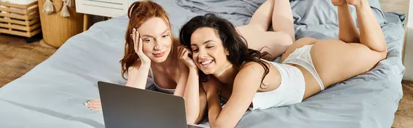 Deux femmes élégantes et aimantes se détendent sur un lit, enveloppées dans un écran d'ordinateur portable. — Photo de stock