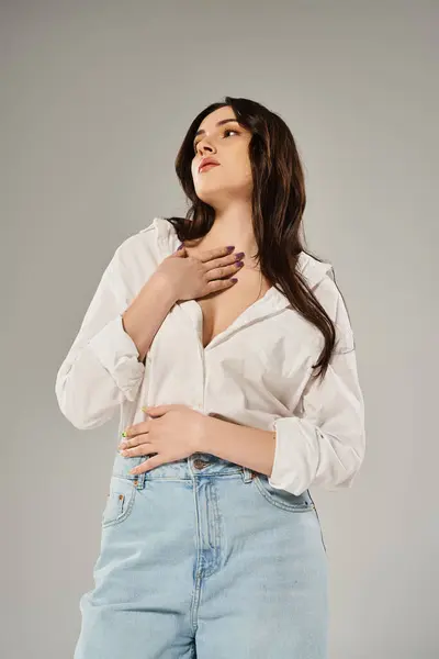 A stunning plus size woman strikes a pose in a trendy white shirt and blue jeans against a neutral gray backdrop. — Stock Photo
