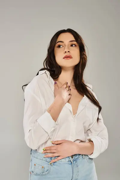 A beautiful plus size woman in a white shirt strikes a graceful pose against a simple gray backdrop. — Photo de stock