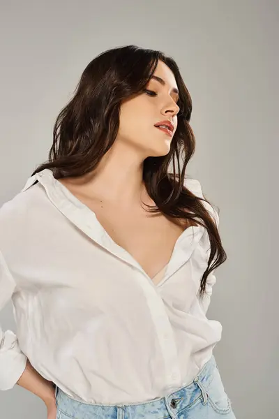 A beautiful plus size woman posing confidently in a white shirt and jeans against a gray backdrop. — Stock Photo