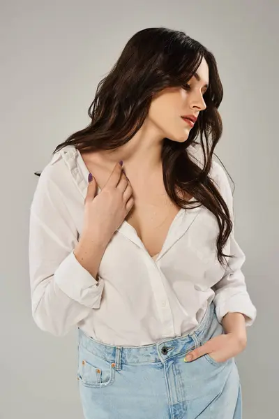 Una bella donna plus-size posa con fiducia in una camicia bianca e jeans su uno sfondo grigio. — Foto stock